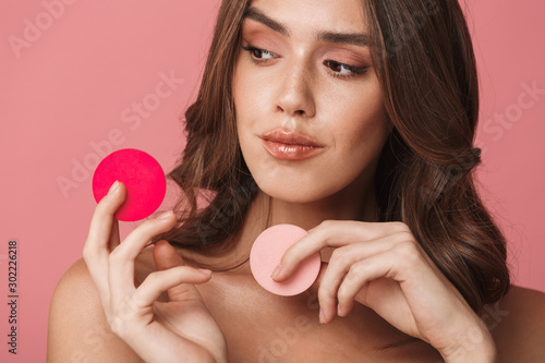 Portrait of beautiful young half-naked woman holding makeup sponges