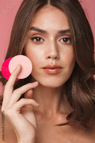 Portrait of slim young half-naked woman holding makeup sponges