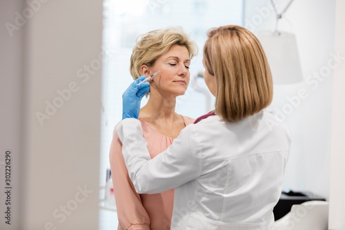 Doctor injecting botox to senior woman patient in clinic