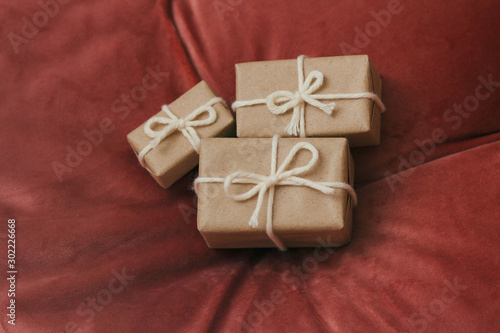 Presents for a Christmas. Gift boxes wrapped in craft paper and tie white string. Red velvet cloth background. Holiday mood. 