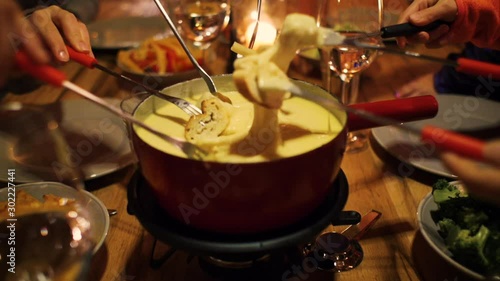 a family enjoying cheese fondue and they stick bread in the melted cheese in a cabin lodge setting photo