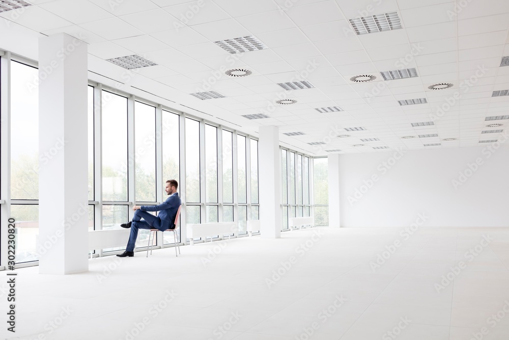 Young attractive businessman sitting while looking through the window in New office