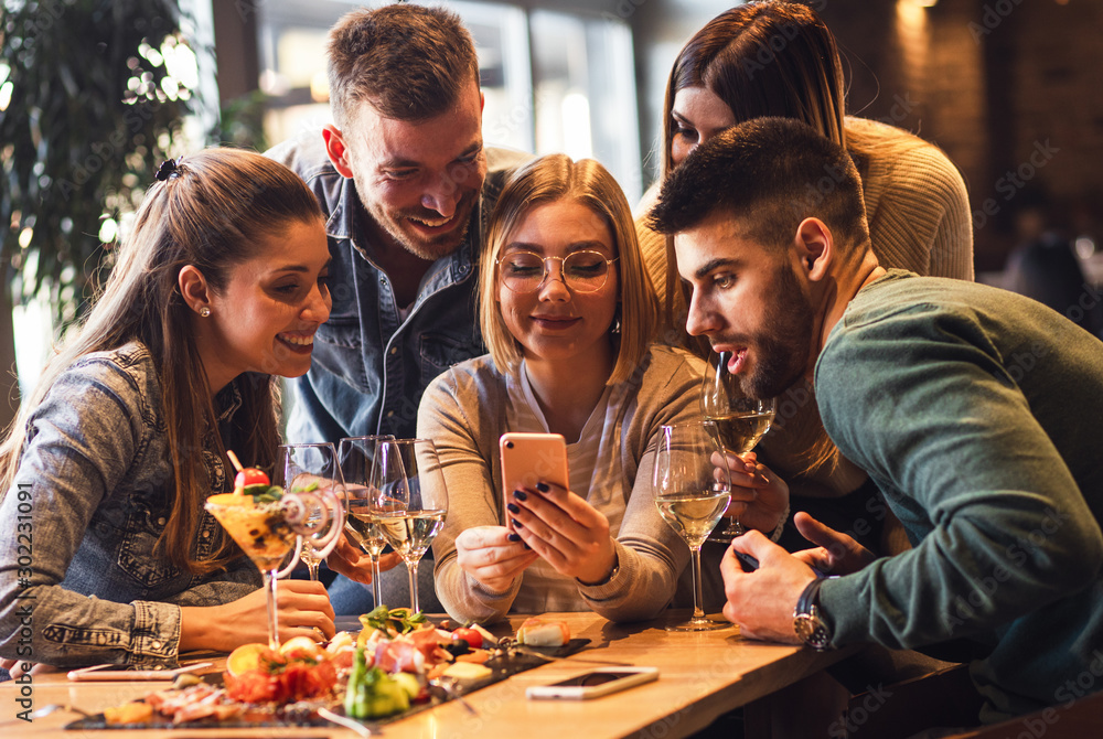 Group of young friends having fun in restaurant talking, laughing while dining at table and making selfie.	 - obrazy, fototapety, plakaty 