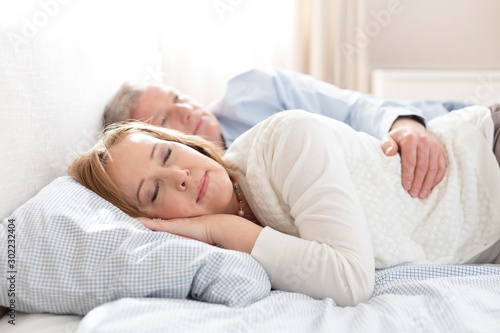 Mature couple sleeping on bed at home