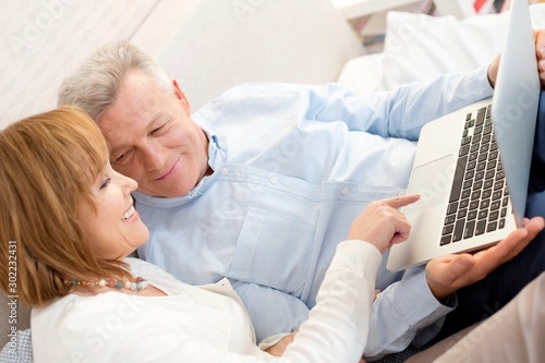 Smiling mature woman pointing at laptop by man in bedroom at home