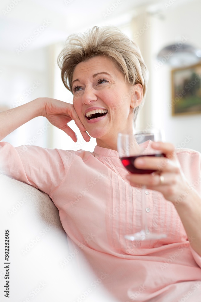 Cheerful mature woman holding wineglass while looking away at home Cheerful mature woman holding wineglass while looking away at home