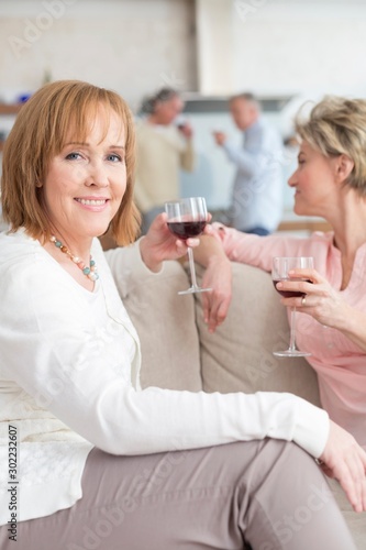 Portrait of mature woman holding drink while sitting by friend on sofa at home