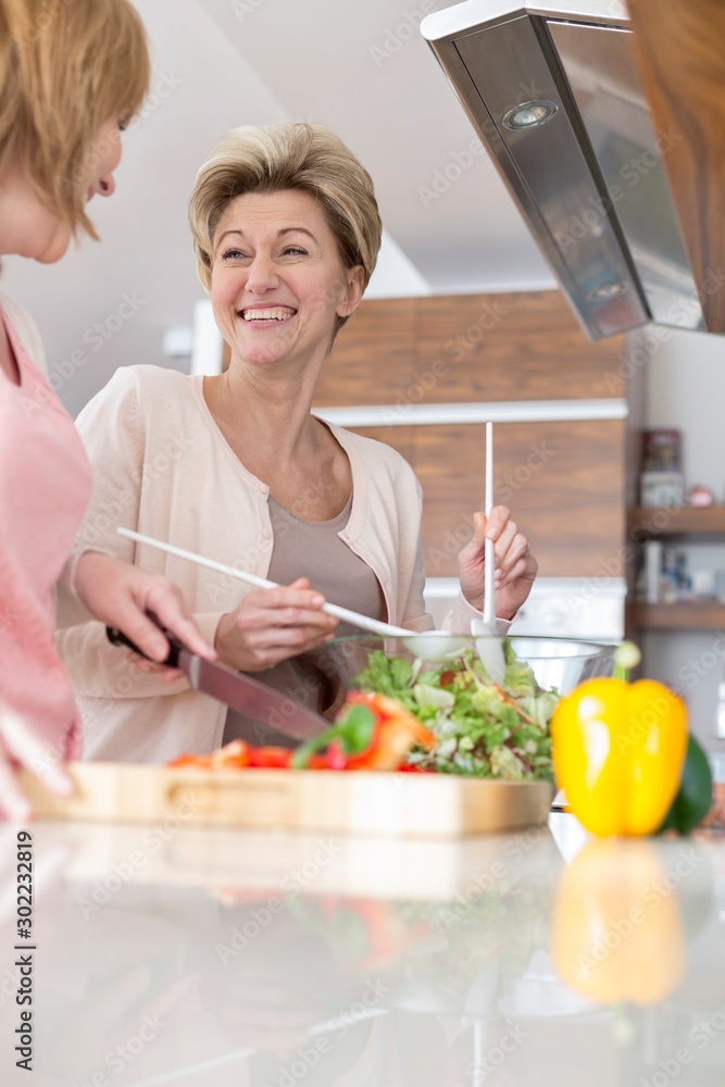 Cheerful mature friends preparing salad in kitchen Cheerful mature friends preparing salad in kitchen
