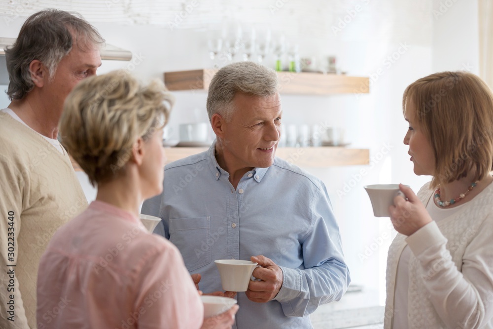 Fototapeta premium Mature friends holding drinks while talking in living room at home