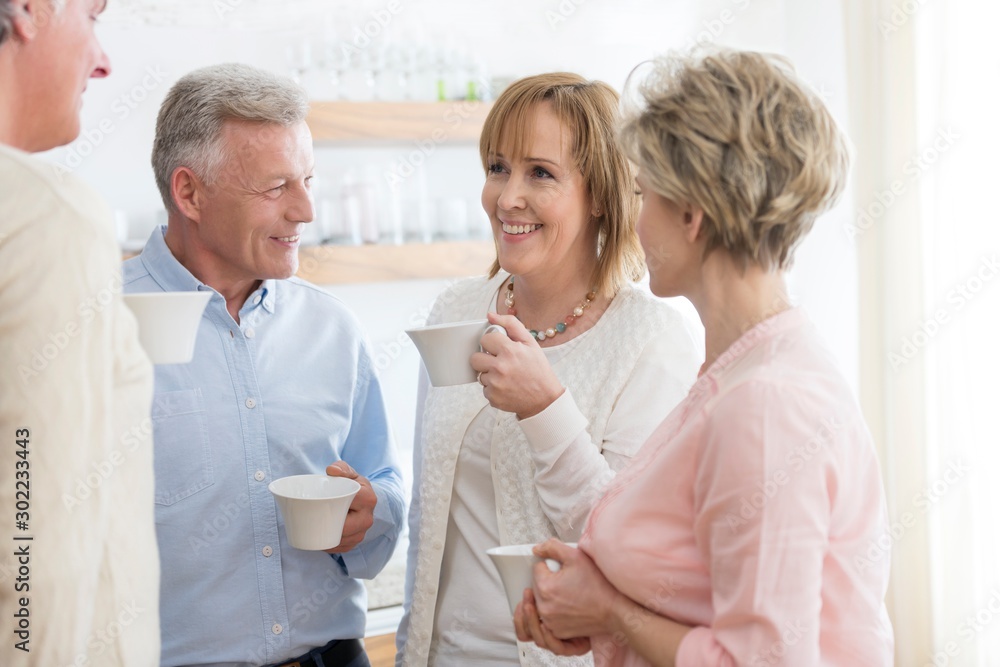 Obraz premium Smiling mature friends holding drinks while talking in living room at home