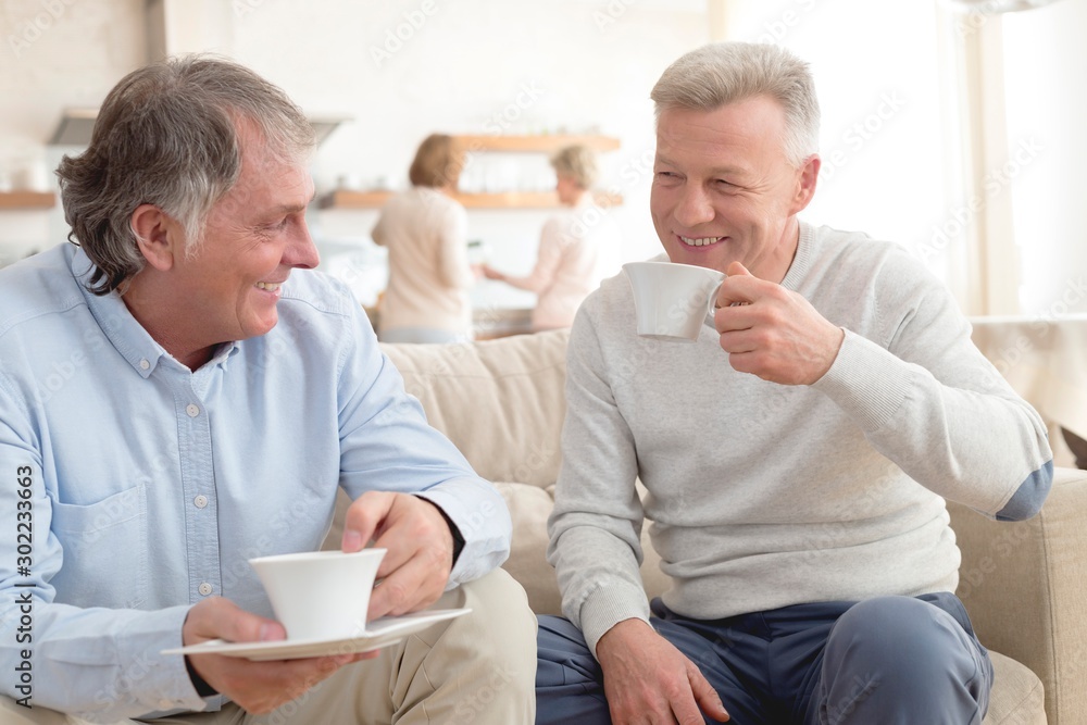 Smiling mature men holding coffee while sitting on sofa at home Smiling mature men holding coffee while sitting on sofa at home