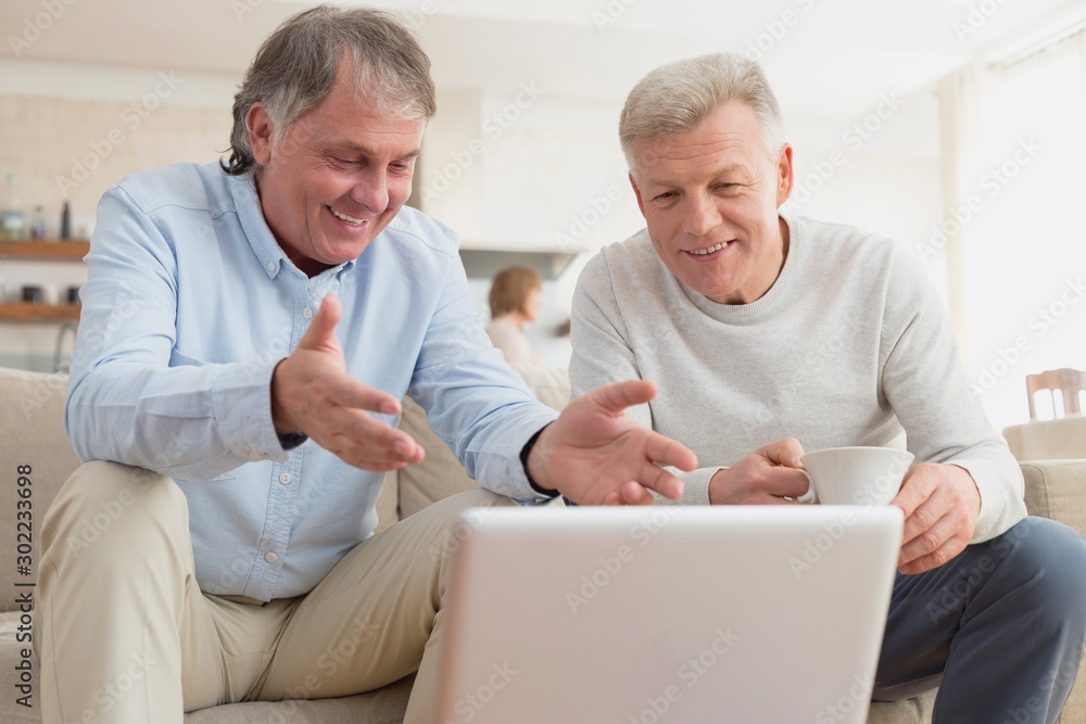 Smiling mature men using laptop while sitting at home Smiling mature men using laptop while sitting at home