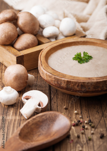 Wooden plate of creamy chestnut champignon mushroom soup with wooden spoon, box with mushroom and kitchen cloth on wooden background.