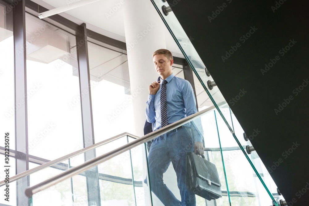 Young attractive businessman walking on stairs with coat on his shoulder at office