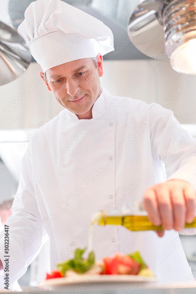Confident mature chef using pouring oil on salad in plate at restaurant Confident mature chef using pouring oil on salad in plate at restaurant