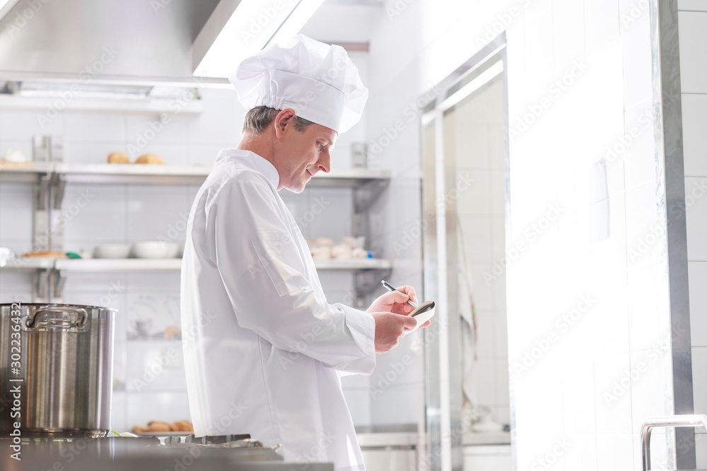 Side view of chef writing on notepad while standing in kitchen at restaurant