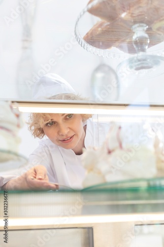 Mature chef arranging fresh cake in display cabinet at restaurant