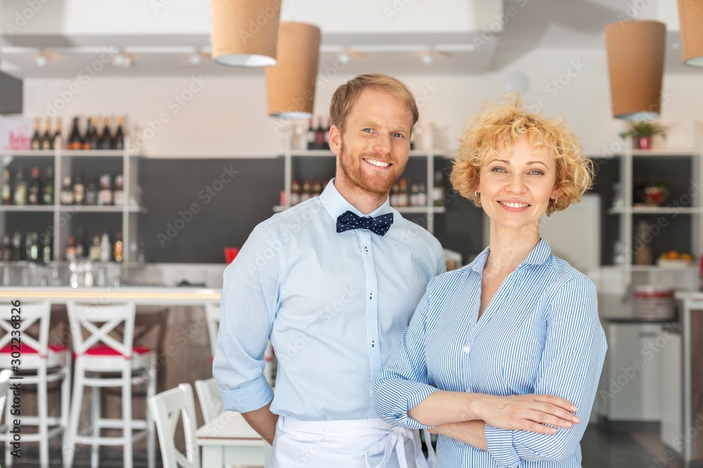 Portrait of smiling owner and waiter standing against furniture at restaurant Portrait of smiling owner and waiter standing against furniture at restaurant