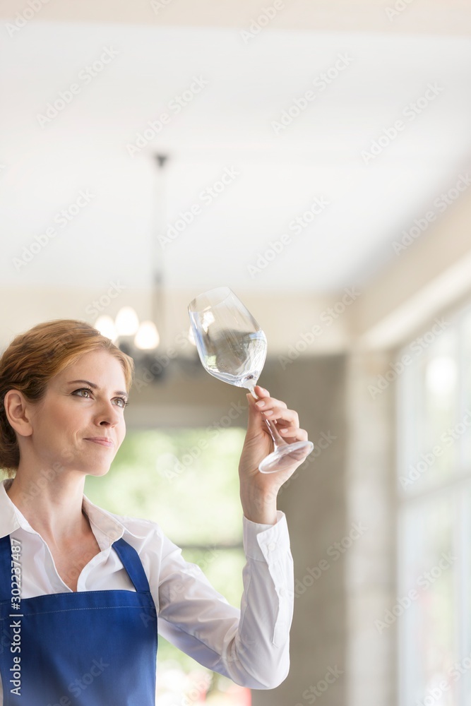 Confident young waitress looking at empty wineglass in restaurant Confident young waitress looking at empty wineglass in restaurant