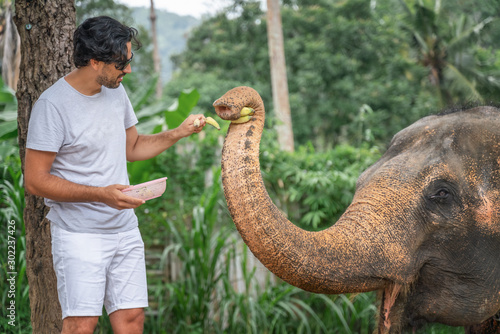Photography Handsome young Latin man tourist is feeding an elephant with bananas in the jung