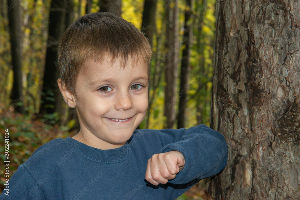 Smiling Young Boy Posing by Tree. Boy posing leaning against a tree in the woods. Smiling Young Boy Posing by Tree. Boy posing leaning against a tree in the woods.