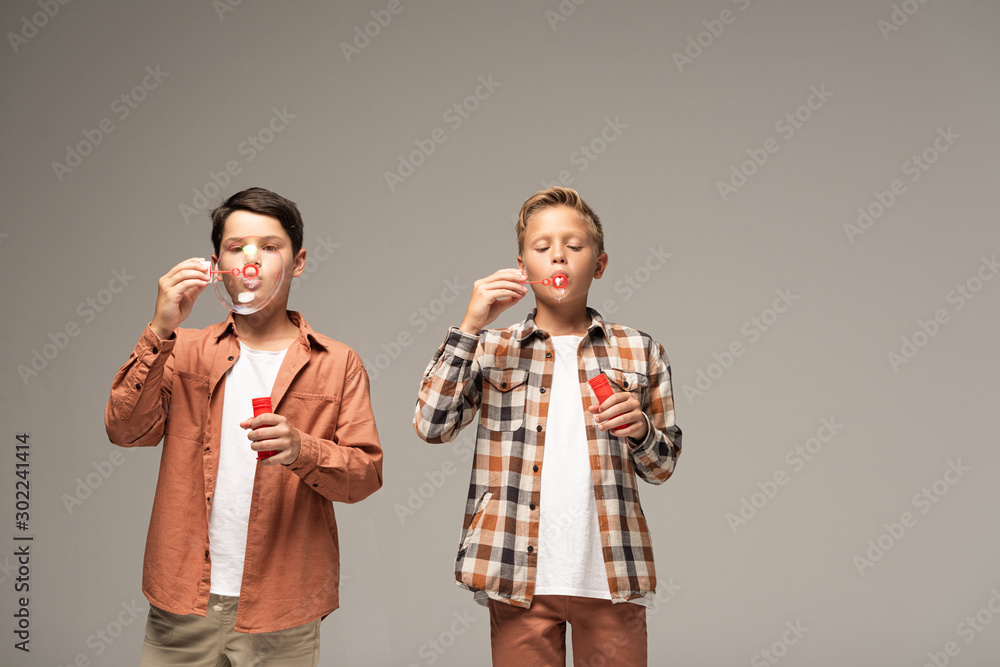front view of two brothers blowing soap bubbles isolated on grey front view of two brothers blowing soap bubbles isolated on grey
