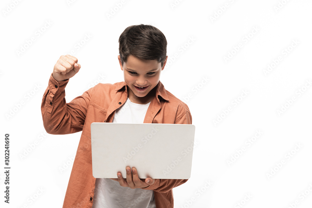 happy boy looking at laptop and showing winner gesture isolated on white