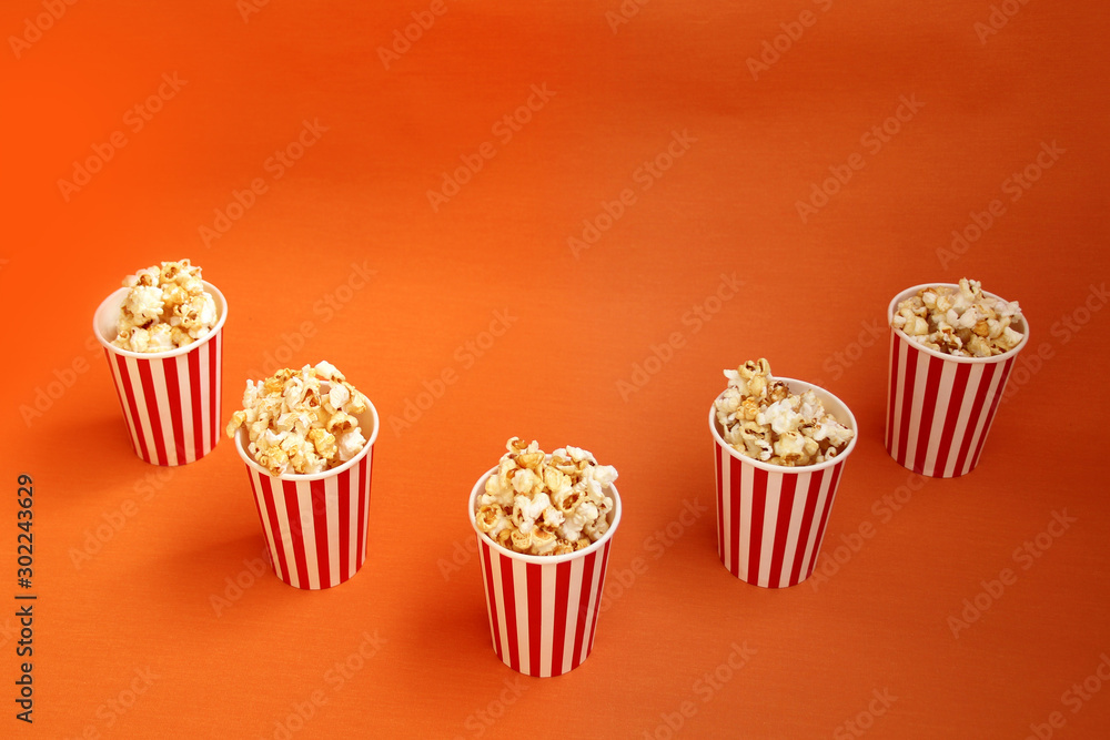 five striped red, white paper cups with popcorn on a bright orange background, close-up, copy space, fast food concept five striped red, white paper cups with popcorn on a bright orange background, close-up, copy space, fast food concept
