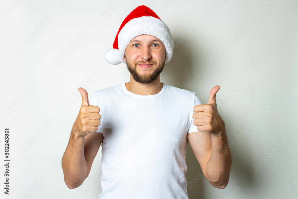 A young man in a Santa Claus hat makes a gesture with his hands on a white background. Christmas concept. Gesture of victory, super A young man in a Santa Claus hat makes a gesture with his hands on a white background. Christmas concept. Gesture of victory, super