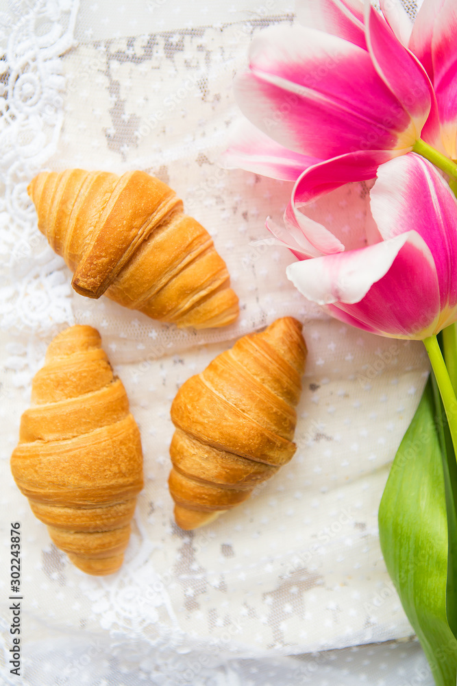 Three croissants and bright pink tulips on lace tablecloth, close-up Three croissants and bright pink tulips on lace tablecloth, close-up