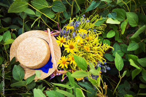 straw hat and basket with flowers stand on the grass, close-up photo