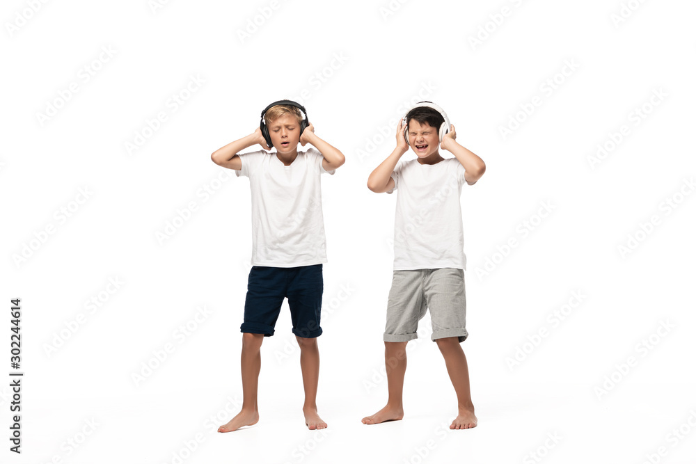 two excited brothers holding hands on headphones while listening music isolated on white two excited brothers holding hands on headphones while listening music isolated on white