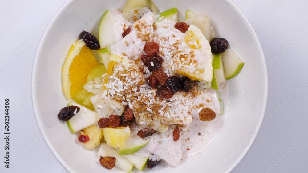 Mixed and assorted fruits in bowl rotating. Top view. Healthy salad dessert. Kiwi, orange, pear and banana slices with yoghurt and raisins. Healthy nutrition Mixed and assorted fruits in bowl rotating. Top view. Healthy salad dessert. Kiwi, orange, pear and banana slices with yoghurt and raisins. Healthy nutrition