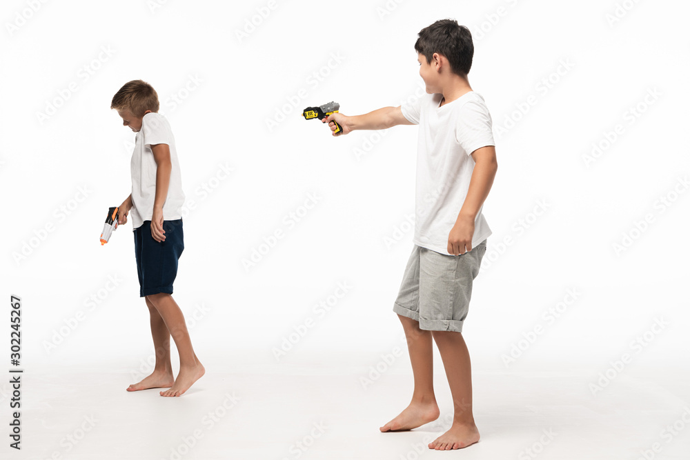 boy aiming with toy gun at scared brother on white background boy aiming with toy gun at scared brother on white background