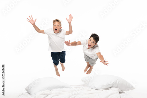 two excited brothers levitating over bed and looking at camera isolated on white