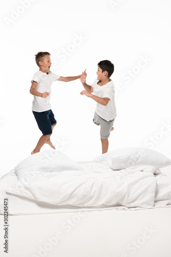 two excited brothers levitating over bed and looking at each other isolated on white