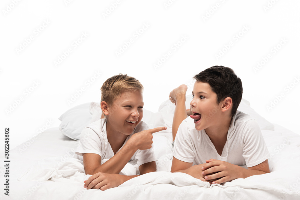 cheerful boy pointing with finger at brother sticking out tongue isolated on white cheerful boy pointing with finger at brother sticking out tongue isolated on white