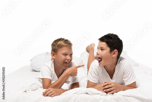 cheerful boy pointing with finger at brother sticking out tongue isolated on white