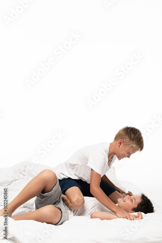 two cheerful boys imitating fighting on bedding isolated on white