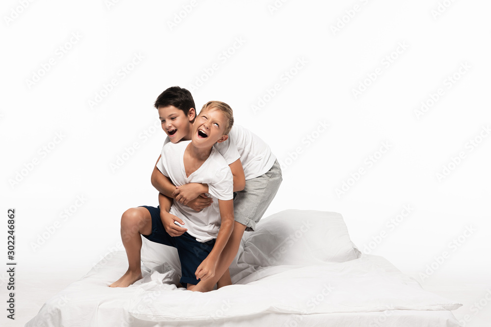cheerful boys imitating fighting while having fun on bed isolated on white cheerful boys imitating fighting while having fun on bed isolated on white