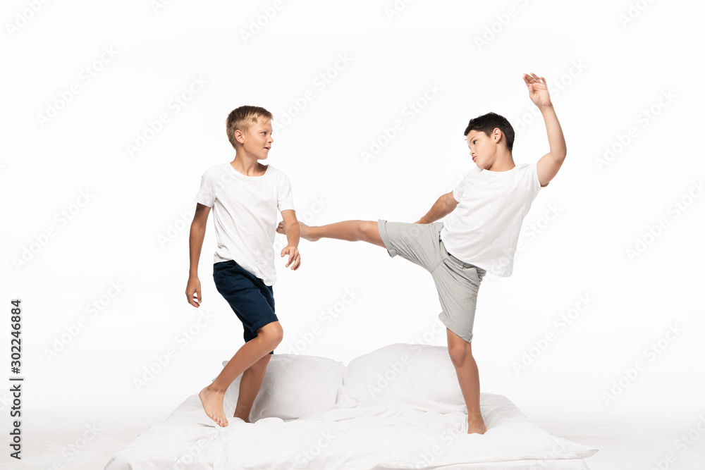 boy jokingly kicking brother with leg while having fun on bed isolated on white boy jokingly kicking brother with leg while having fun on bed isolated on white