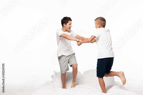 two brothers fighting for fun white standing on bed isolated on white