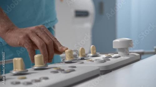 Surgeon operates robotic diagnostic system via remote control panel, nurse in background, hospital, operating roon, hands close-up photo