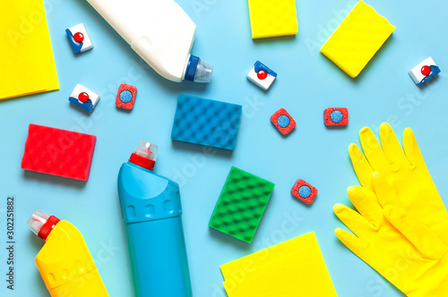 House cleaning concept. Household chemicals, disinfectant, bleach, antibacterial gel, yellow rubber gloves, sponge, rags, dishwasher tablets on blue background. Flat lay top view. Cleaning accessories