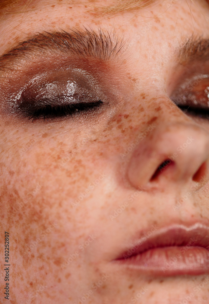 Obraz premium Closeup macro portrait of female face. Human woman half-face with day beauty makeup. Girl with perfect skin and freckles.