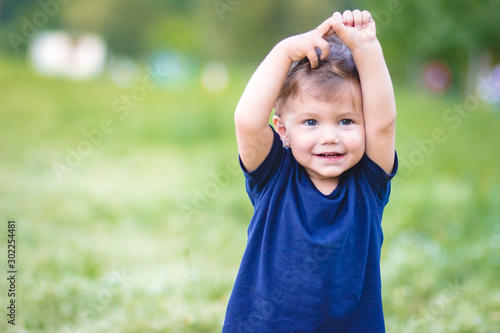 Cute little blond boy in blue t-shirt standing with hands above his head.