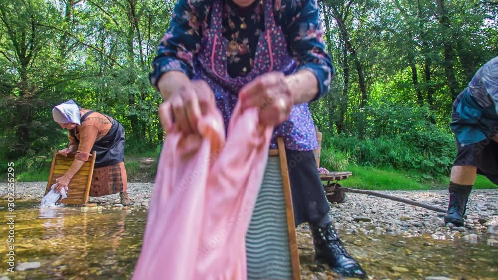 Older washerwomen are washing laundry in the river. This is how they
