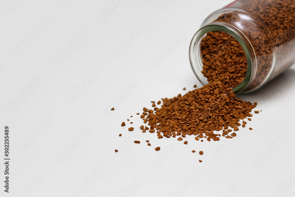 Open glass jar with instant coffee spilled out. White solid background. Open glass jar with instant coffee spilled out. White solid background.
