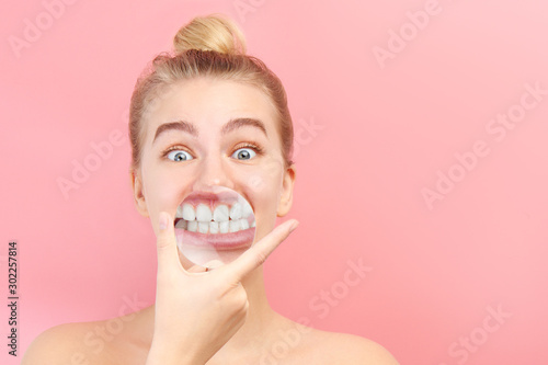 Young beautiful woman with magnifier demonstrates snow-white smile  healthy teeth. Funny dental concept  stomatology clinic patient isolated on pink background