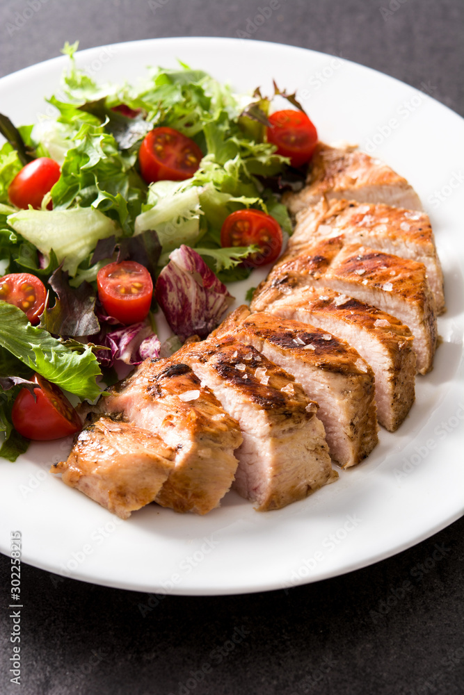 Grilled chicken breast with vegetables on a plate on black background Grilled chicken breast with vegetables on a plate on black background